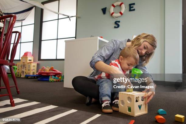 woman and boy playing with geometric puzzle box at preschool - babysit stockfoto's en -beelden