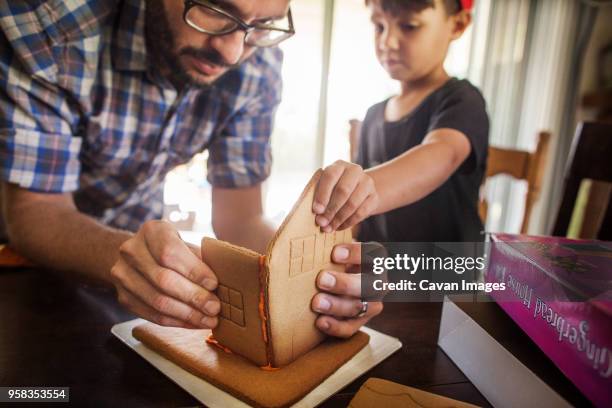 father and son making gingerbread house at home - gingerbread house stock-fotos und bilder