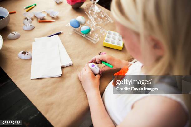 high angle view of girl decorating easter egg on table at home - paper decoration stock-fotos und bilder