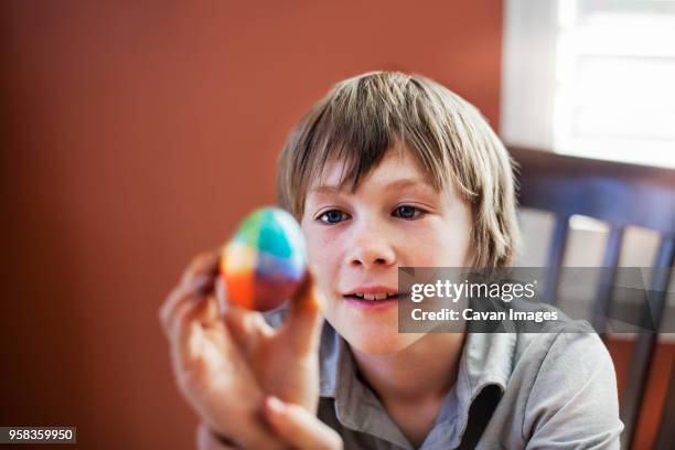 boy looking at decorated easter egg while sitting on chair at home - egg chair stockfoto's en -beelden