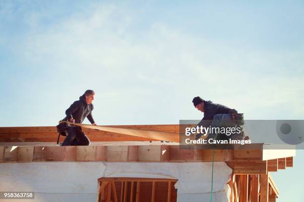 workers constructing roof beam against sky during sunny day - craftsman stock-fotos und bilder