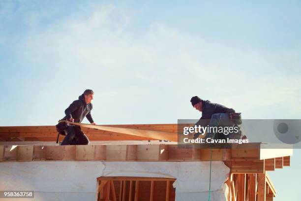 workers constructing roof beam against sky during sunny day - artisan photos et images de collection