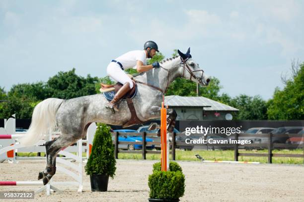 side view of man riding horse over hurdle against sky - jockey uniform stock pictures, royalty-free photos & images