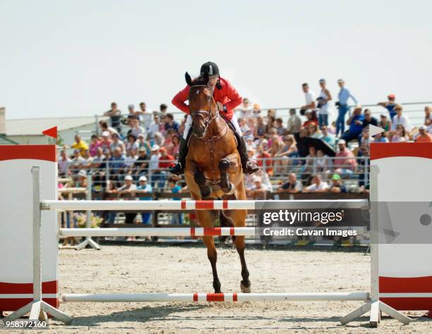 man riding horse while jumping on hurdle at sport event - concurso de saltos ecuestres fotografías e imágenes de stock