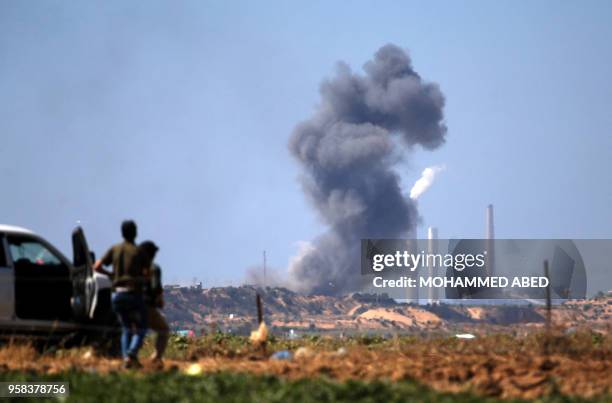 Palestinians look at smoke billowing from the site of an Israeli air strike on a Hamas' military site in Beit Lahia near the border between Israel...