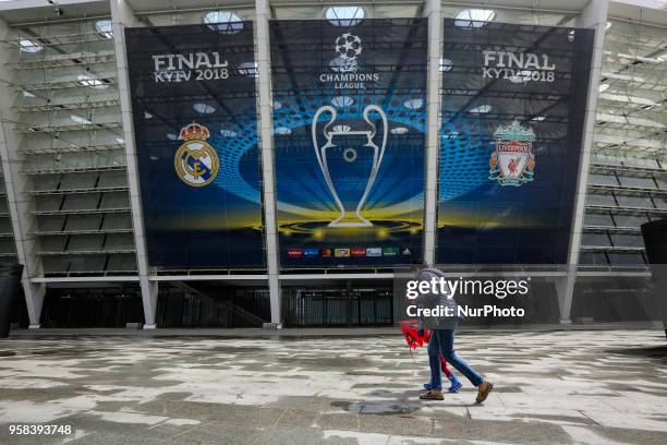 Woman and a kid under the umbrella walk past NSC Olimpiyskiy Stadium covered with banners for the Champions League in Kyiv, Ukraine, May 14, 2018....