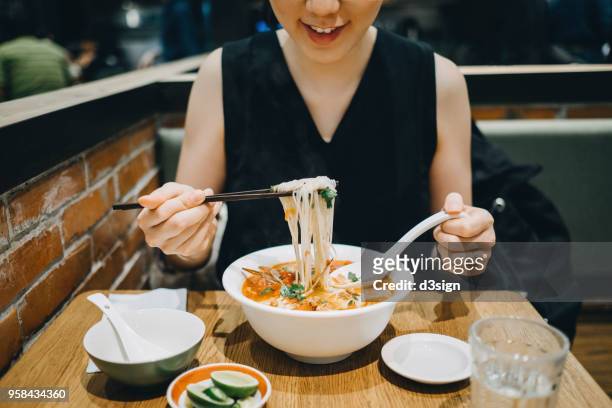 asian woman eating soup noodles joyfully in restaurant - eating spicy food stock pictures, royalty-free photos & images
