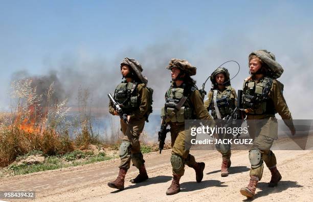 Israeli soldiers walk amidst smoke from a fire in a wheat field near the Kibbutz of Nahal Oz, along the border with the Gaza Strip, on May 14, 2018...