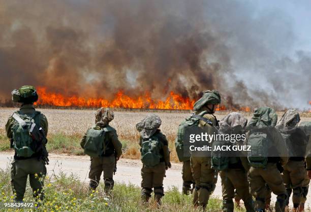 Israeli soldiers walk amidst smoke from a fire in a wheat field near the Kibbutz of Nahal Oz, along the border with the Gaza Strip, on May 14, 2018...