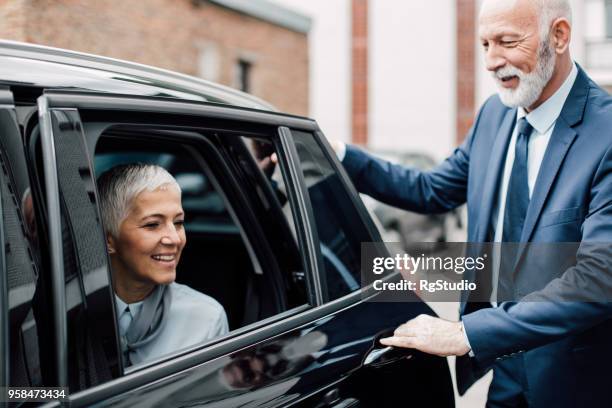 senior gentleman opening car door for mature business woman - car door stock pictures, royalty-free photos & images