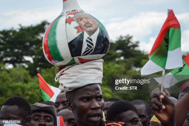 Supporter of Burundi's ruling CNDD-FDD party, balances a gourd on his head with the image of the Burundian President Pierre Nkurunziza, during a...
