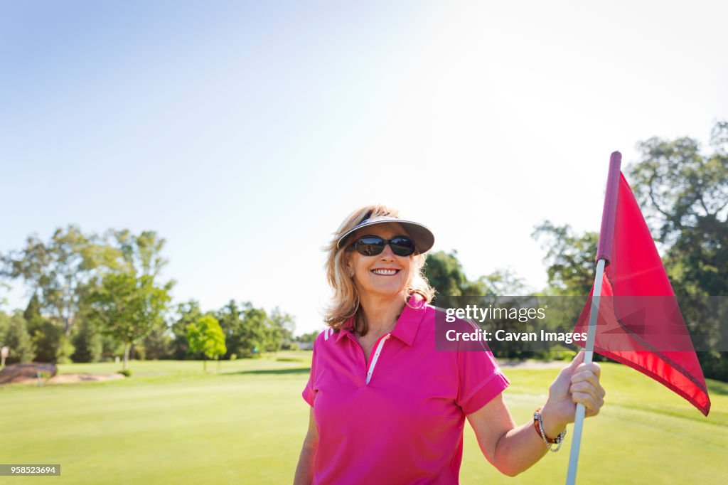 Portrait of happy woman holding flag while standing at golf course against clear sky