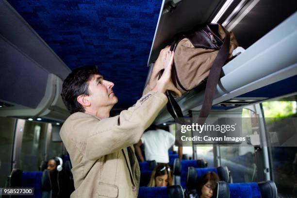 man putting bag in luggage rack while standing in bus - gepäckablage stock-fotos und bilder
