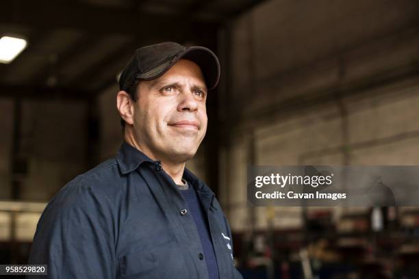 portrait of mechanic standing by bus in repair shop - arbeider stockfoto's en -beelden