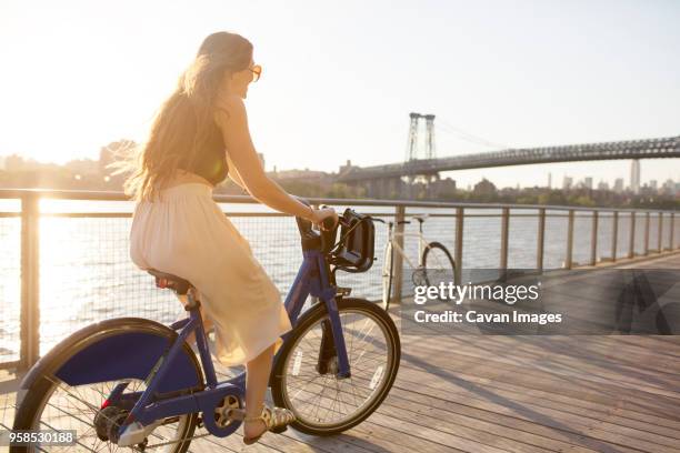 happy woman riding bicycle on promenade during sunset - promenade seafront stock pictures, royalty-free photos & images