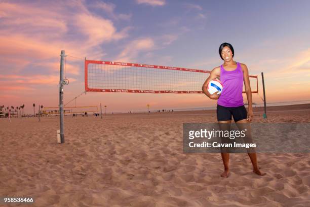 portrait of woman holding volleyball while standing at beach - womens volleyball stock-fotos und bilder