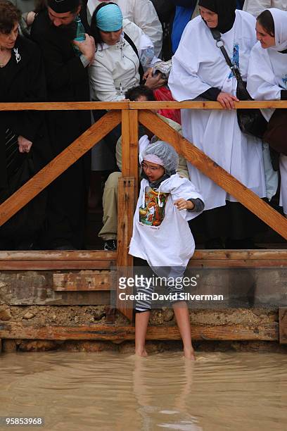 Young Christian girl cries out as her father lowers her into the water to baptize her during Epiphany celebrations by the Jordan River on January 18,...