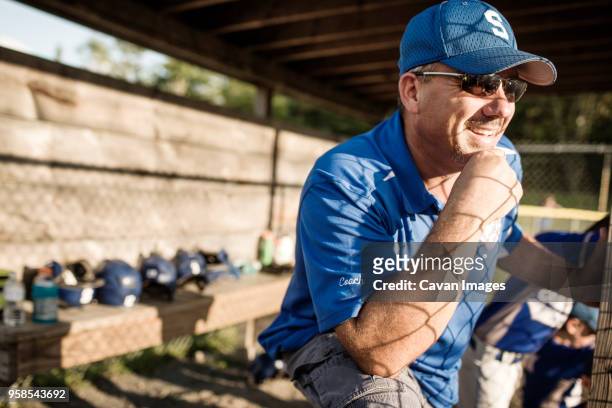 coach smiling while standing in dugout - dugout baseball stock pictures, royalty-free photos & images