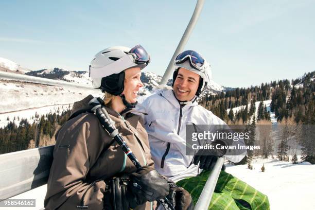 happy couple sitting in ski lift against clear sky - couple ski lift stockfoto's en -beelden