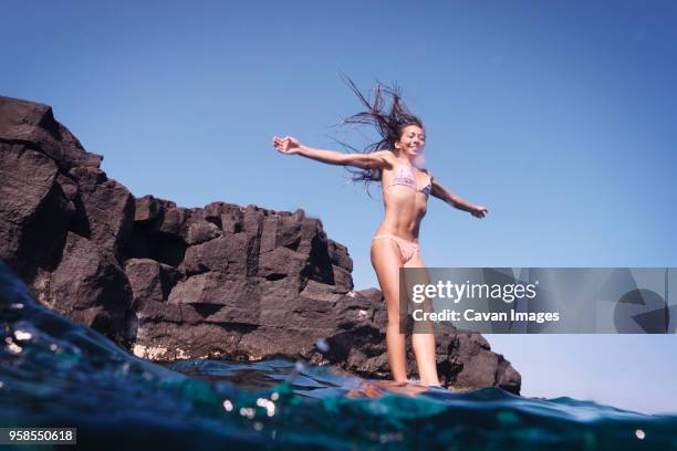 smiling woman with arms outstretched jumping into water - klippe stock-fotos und bilder