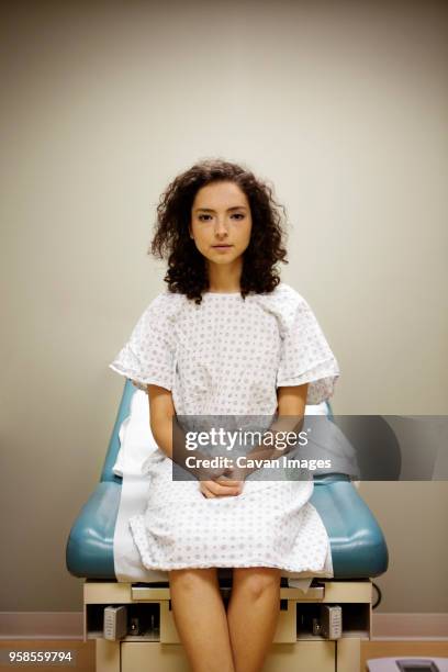 portrait of woman with hands clasped sitting on bed in hospital - tavolo da visita foto e immagini stock