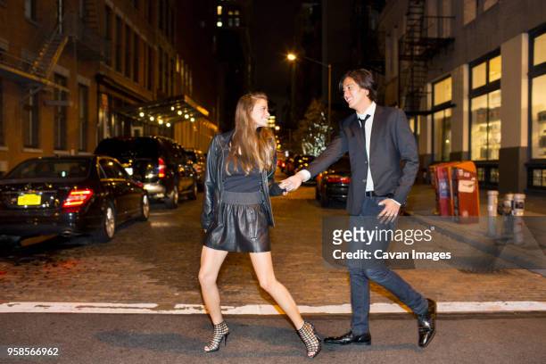 cheerful couple holding hands and walking on city street at night - smart casual stock pictures, royalty-free photos & images