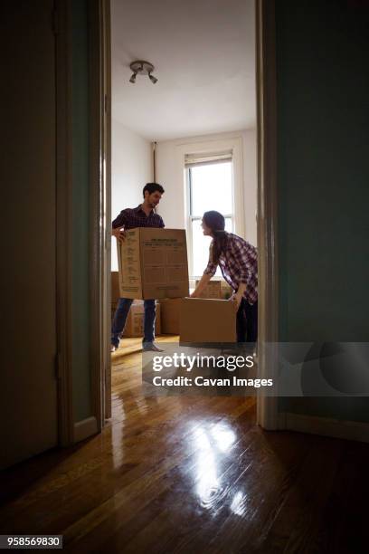 couple carrying boxes in new home seen through doorway - new boyfriend stock pictures, royalty-free photos & images