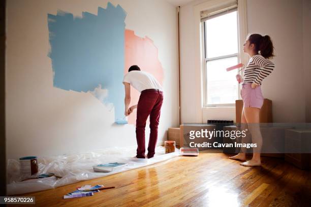 woman hand on hip looking at man painting on wall - ペンキローラー ストックフォトと画像