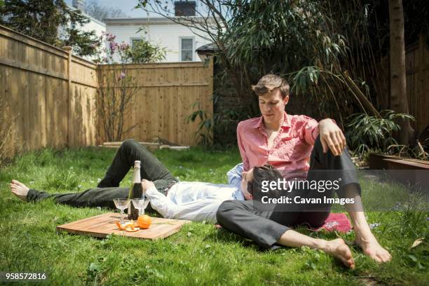 gay couple relaxing on field in backyard - mann lässig gras sitzen stock-fotos und bilder