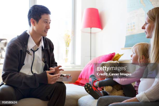doctor talking with woman while sitting on sofa at home - house call stockfoto's en -beelden