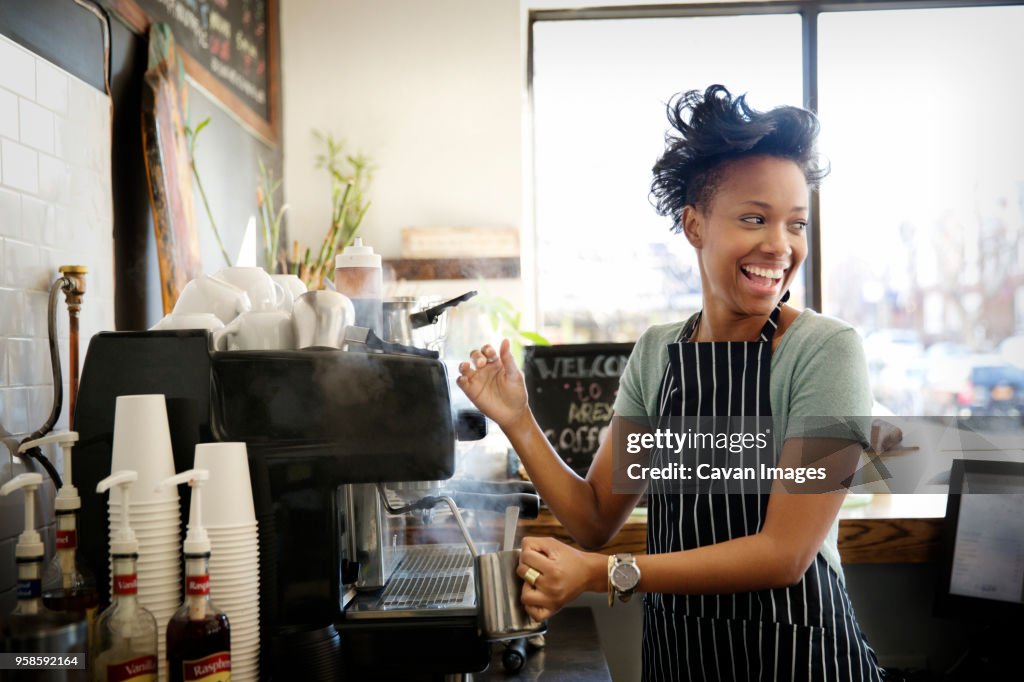 Happy woman looking away while making coffee in cafe