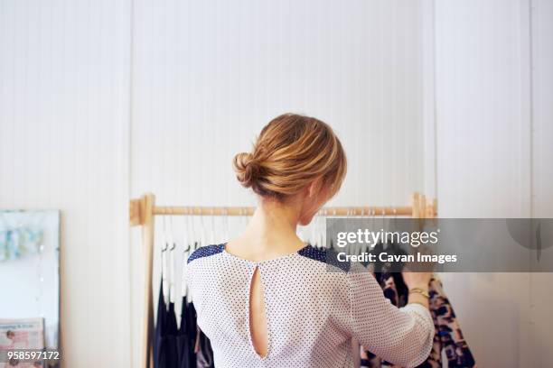 rear view of woman arranging clothes in rack - haarknoten stock-fotos und bilder