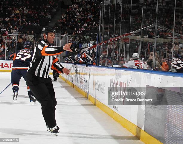 Referee Dan Marouelli takes a stick out of a crack in the glass during the game between the New Jersey Devils and the New York Islanders at the...