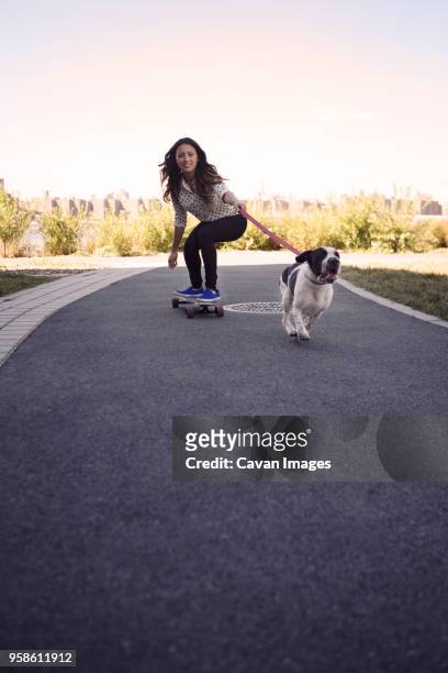 woman skateboarding with running dog on street against clear sky - dog skateboard stock pictures, royalty-free photos & images