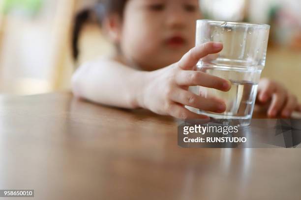 baby girl hand holding glass of water on table - glass of water hand ストックフォトと画像
