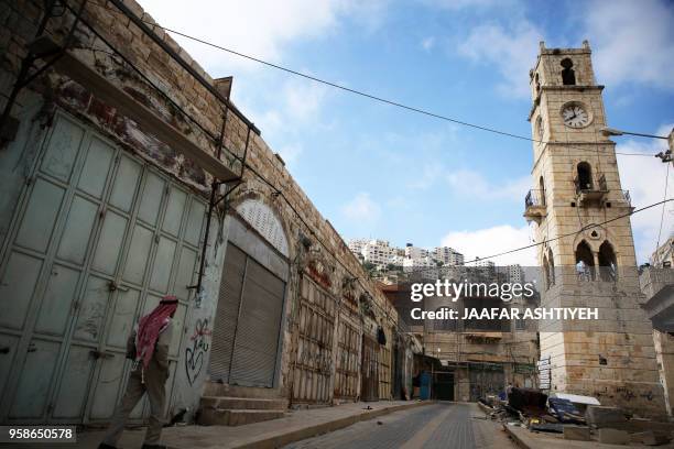 Palestinian man walks past closed shops on an empty street in the Israeli occupied West Bank city of Nablus on May 15 during a general strike called...