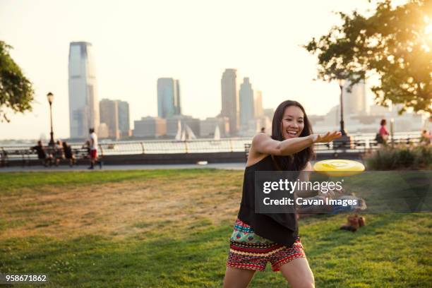happy woman catching plastic disc while standing in park against clear sky - frisbee fotografías e imágenes de stock