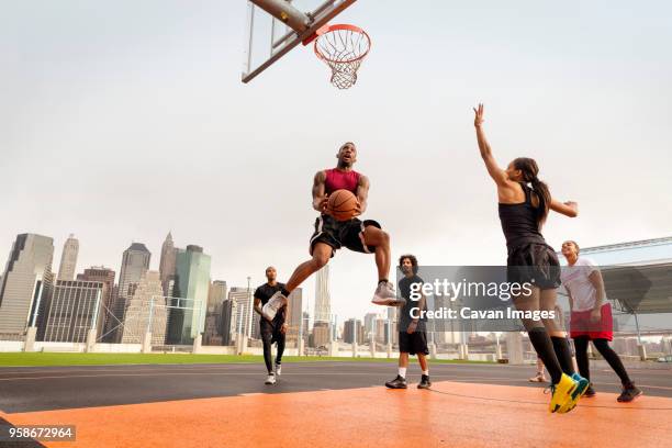 athletes playing basketball in court against buildings - basketballmannschaft stock-fotos und bilder