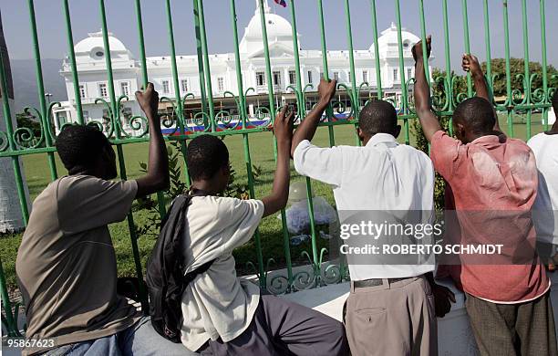 Haitian men hold on to the front fence bars of the Presidential Palace in Port-Au-Prince, Haiti 12 May 2006 as they watch workers build a stage. Rene...