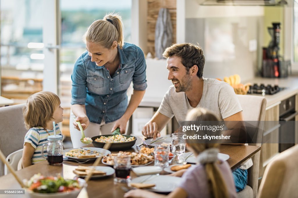 Young happy woman serving lunch to her family at dining table.