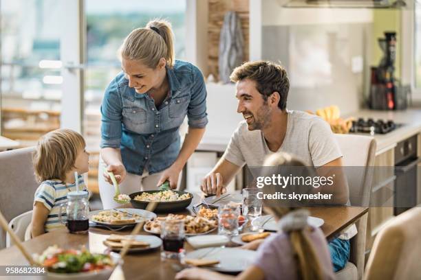 young happy woman serving lunch to her family at dining table. - dining table stock pictures, royalty-free photos & images