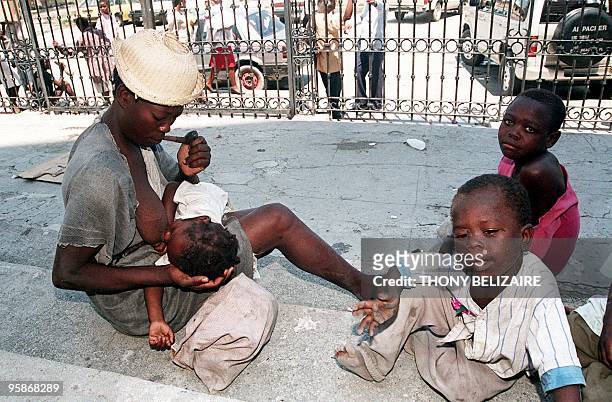 Poor Haitian woman smoking a pipe feeds her baby 25 May in front of the Port-au-Prince Cathedral accompanied by her other children. In the Cathedral,...