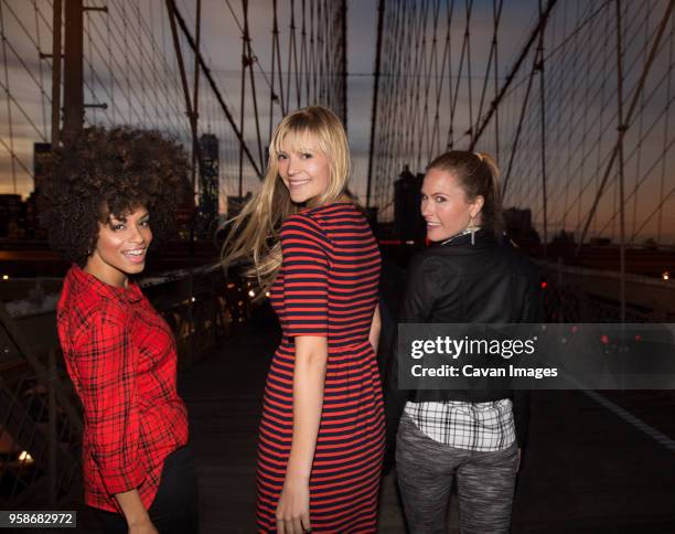 women looking over shoulder while walking on brooklyn bridge - regarder par dessus son épaule photos et images de collection