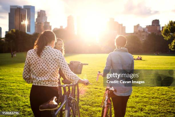 rear view of women walking with bicycles on field in central park - adult riding bike through park stock pictures, royalty-free photos & images