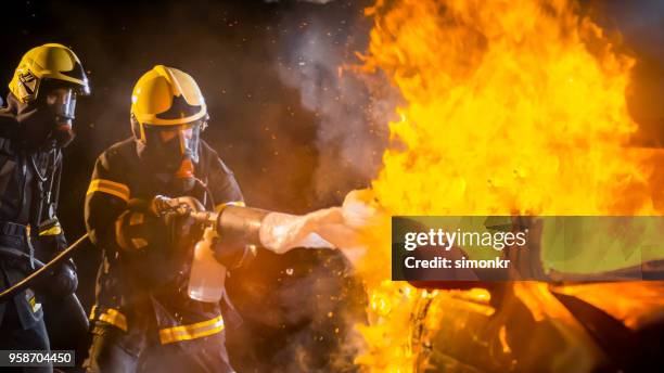 brandweerlieden brandbestrijding schuim op het verbranden van auto spuiten - uitgaan stockfoto's en -beelden