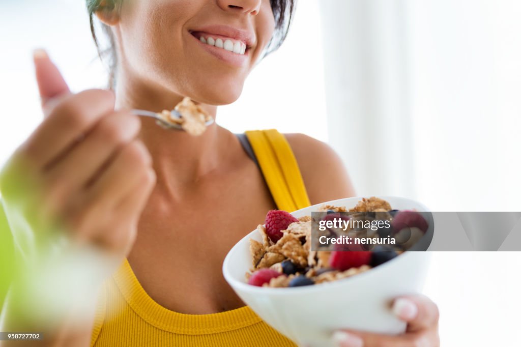 Beautiful young woman eating cereals and fruits at home.