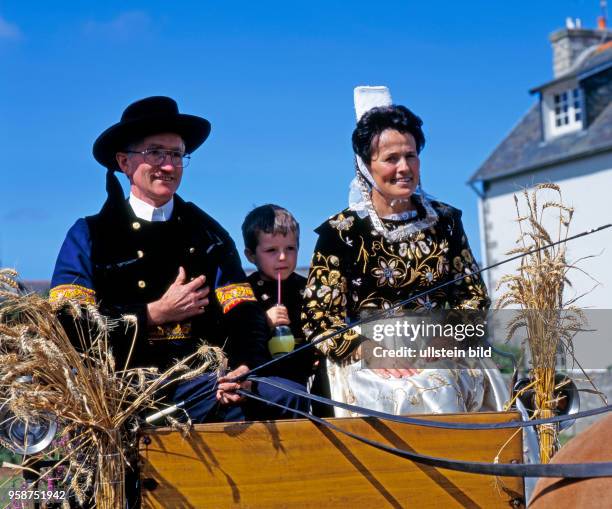 Bretonische Familien auf geschmueckter Kutsche und in traditioneller bretonischer Tracht, die in der Landschaft Finistere nur noch zu festlichen...