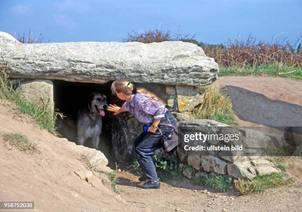 Junge Frau erschrickt vor Irischem Wolfshund, der den Eingang zur megalithischen Grabkammer, Dolmen des Pierres Plates, in Locmariaquer in der...