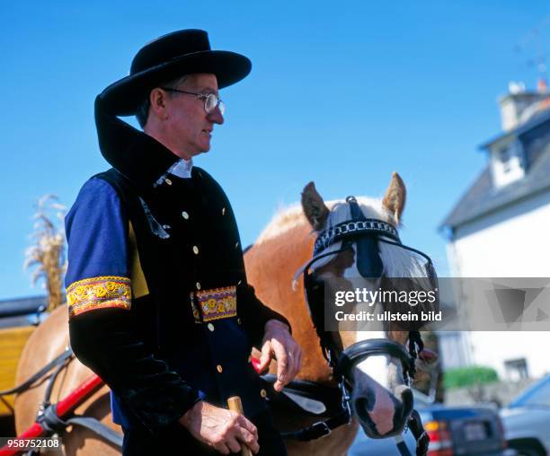 Bretonischer Landwirt mit Pferd und geschmueckter Kutsche in traditioneller bretonischer Tracht, die in der Landschaft Finistere nur noch zu...
