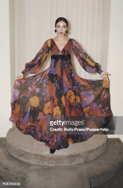 Young female model wears a long empire line maxi dress in silk organdie printed in red, orange, black and violet with pleated layers and puffed...